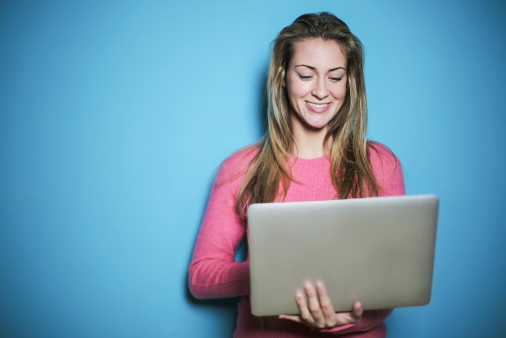 Young woman smiling while using a laptop, set against a blue background, representing digital engagement and online services.
